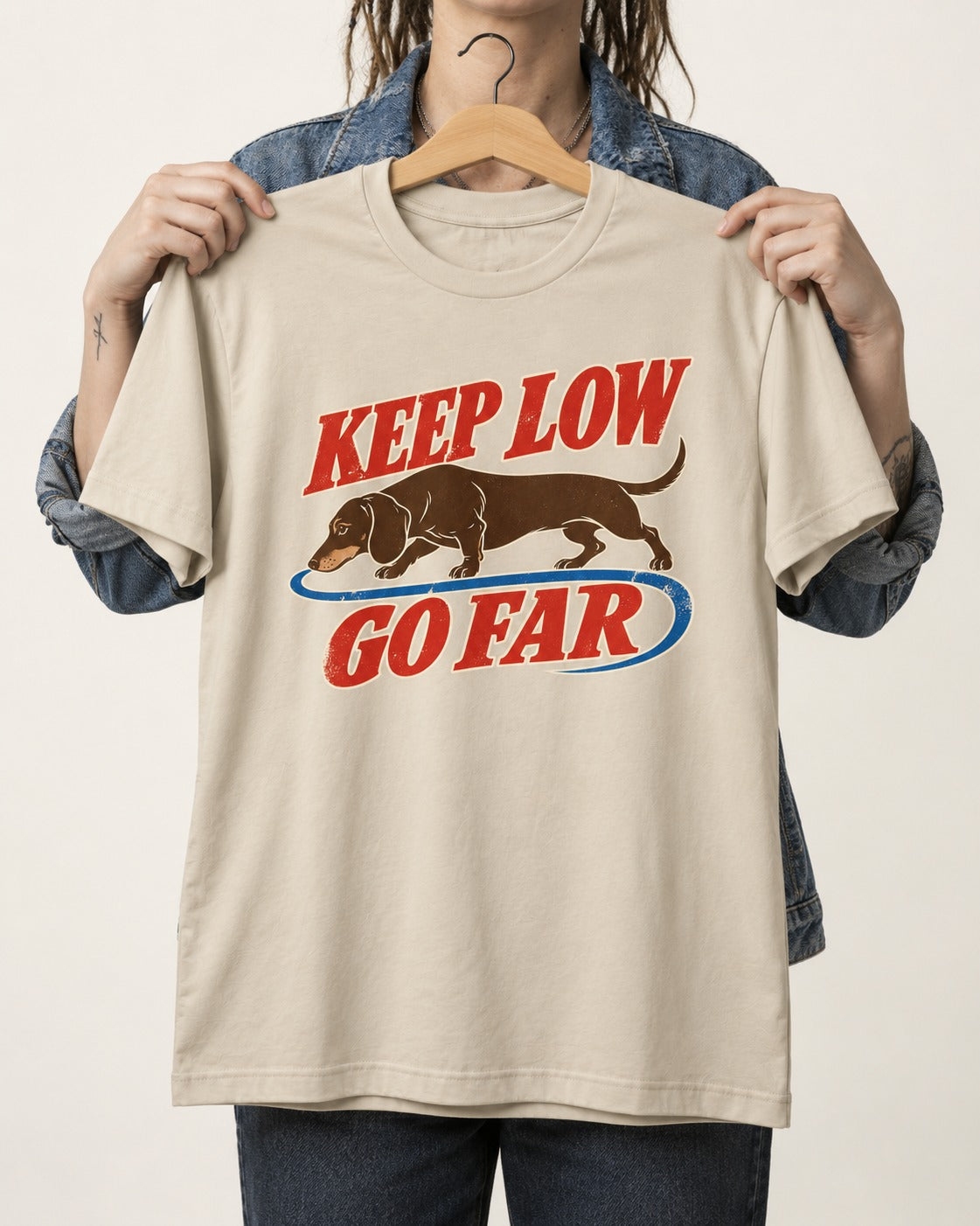 Dachshund Keep Low Go Far T-Shirt in Sand, held up on a hanger