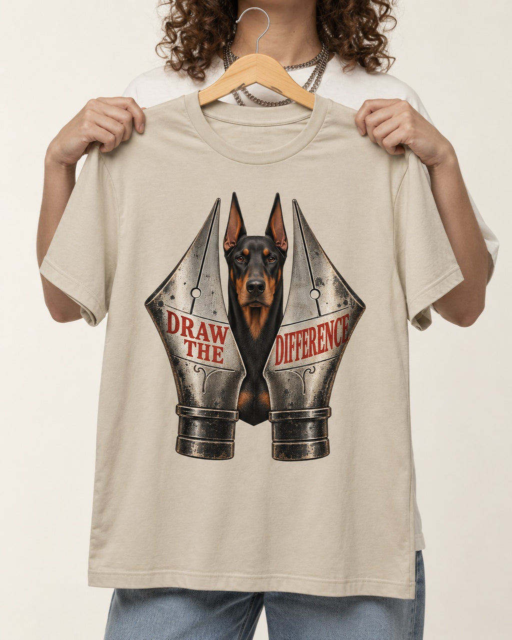 Doberman Draw the Difference T-Shirt in Sand, held up on a hanger