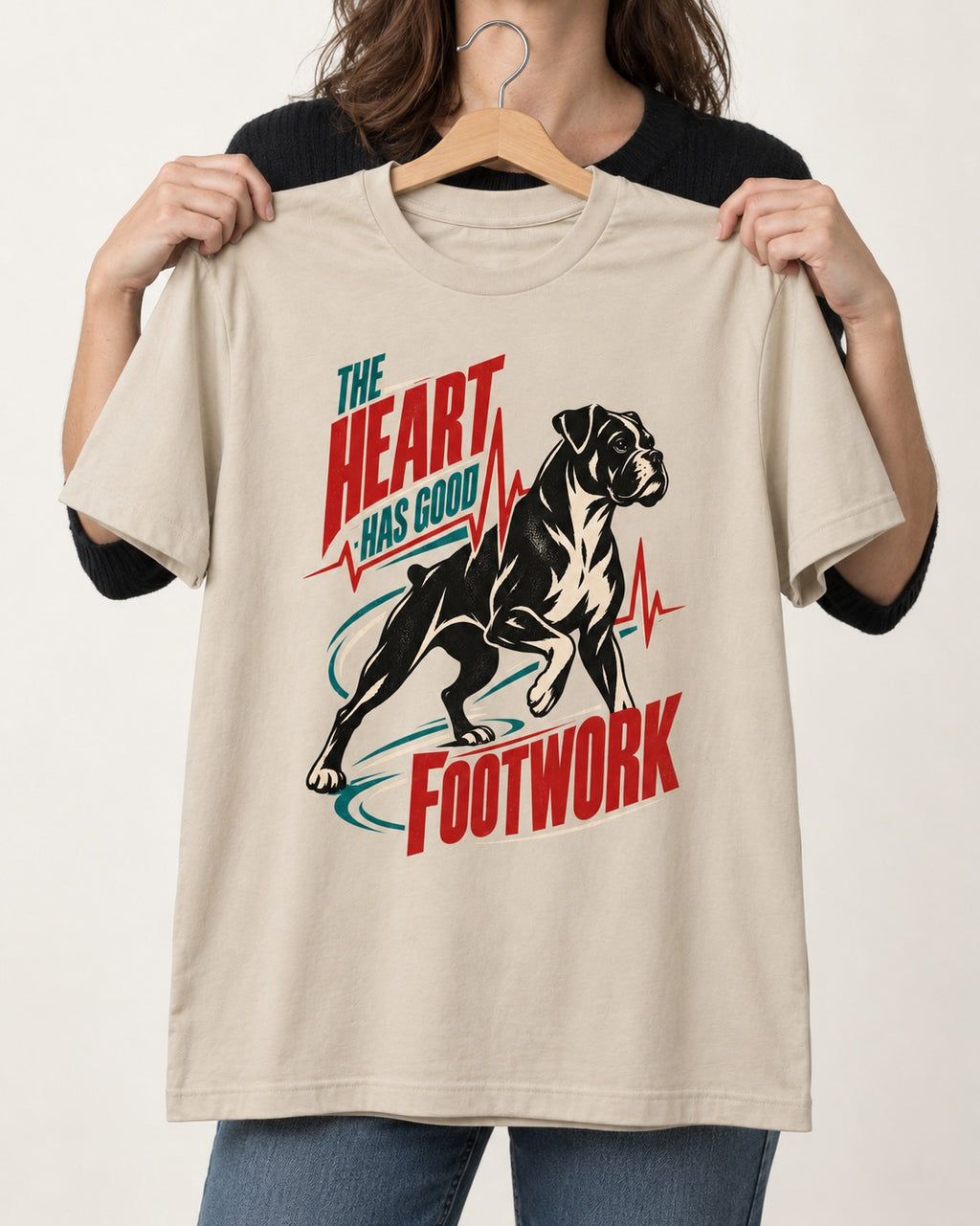 Boxer Heart Has Good Footwork T-Shirt in Sand, held up on a hanger
