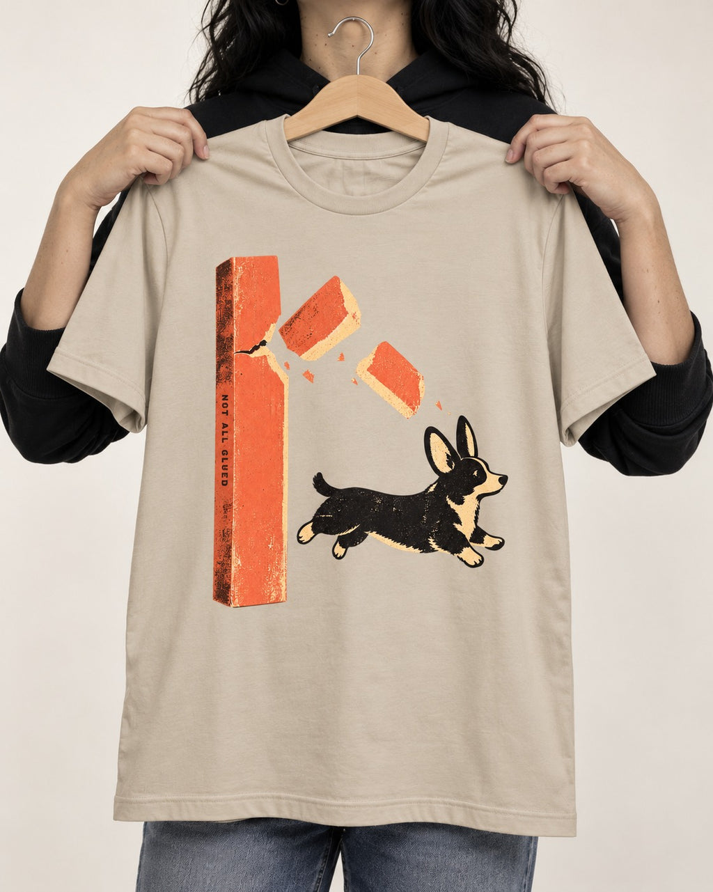 Not All Glued Corgi T-Shirt in Sand, held up on a hanger