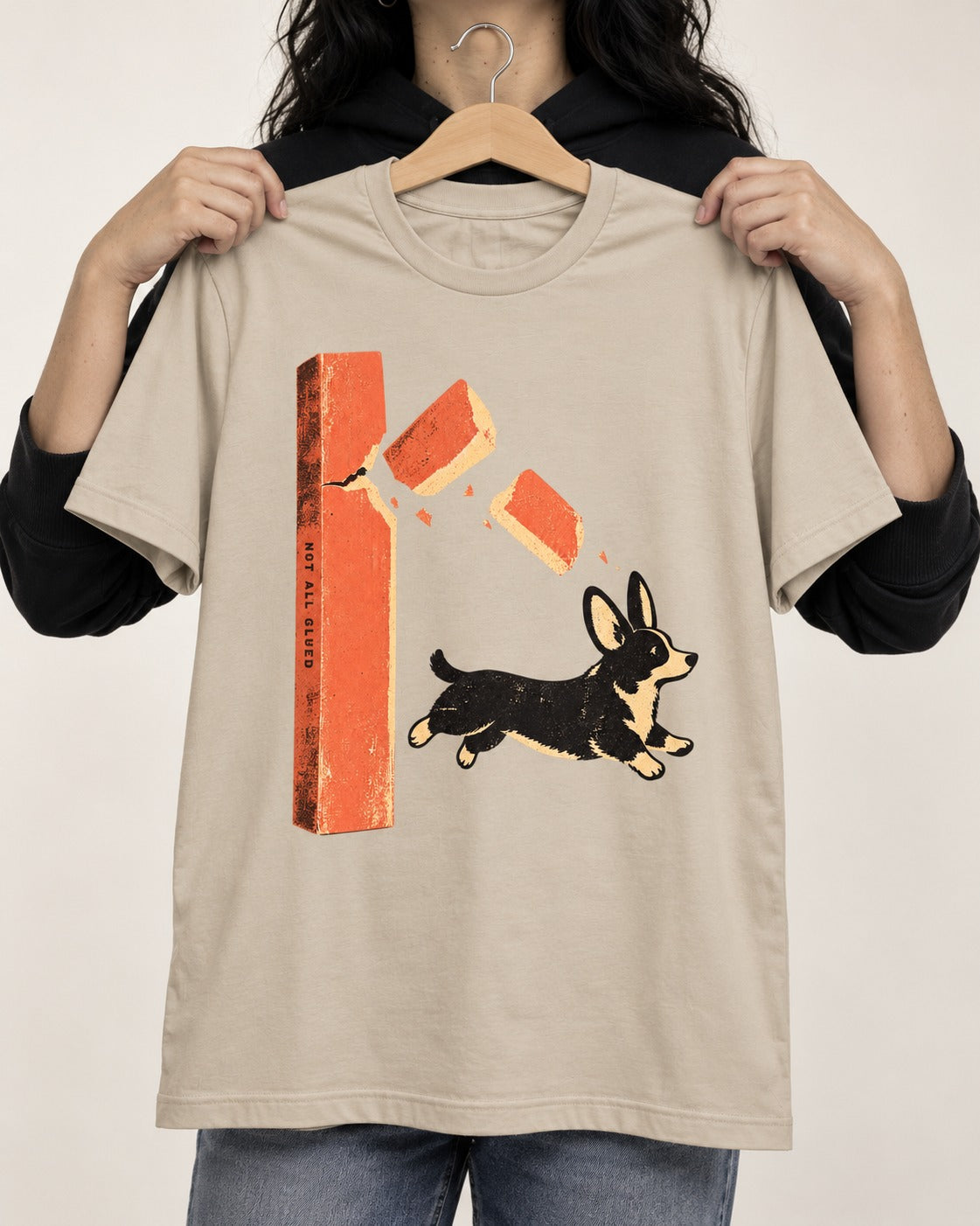 Not All Glued Corgi T-Shirt in Sand, held up on a hanger