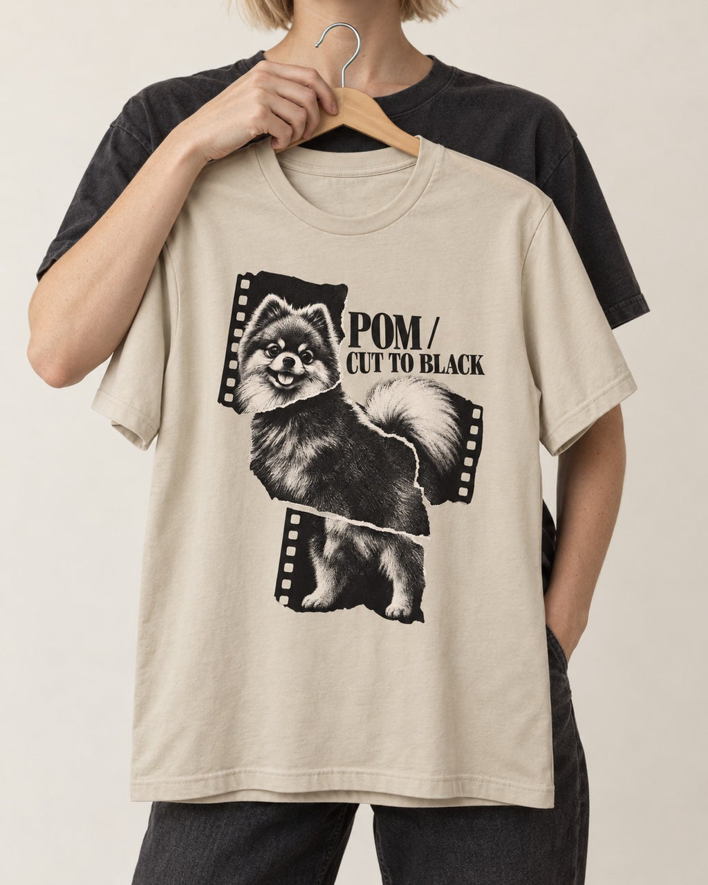 Pomeranian Cut to Black T-Shirt in Sand, held up on a hanger