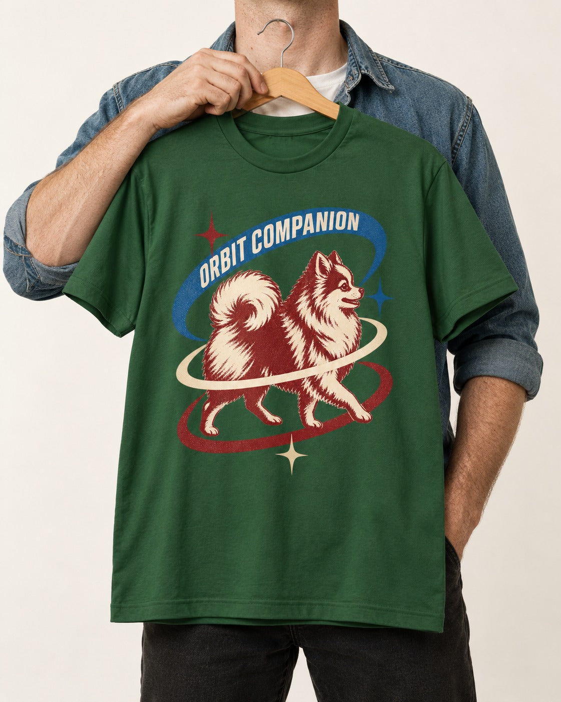 Pomeranian Orbit Companion Retro Space Graphic T-Shirt in Forest Green, held up on a hanger