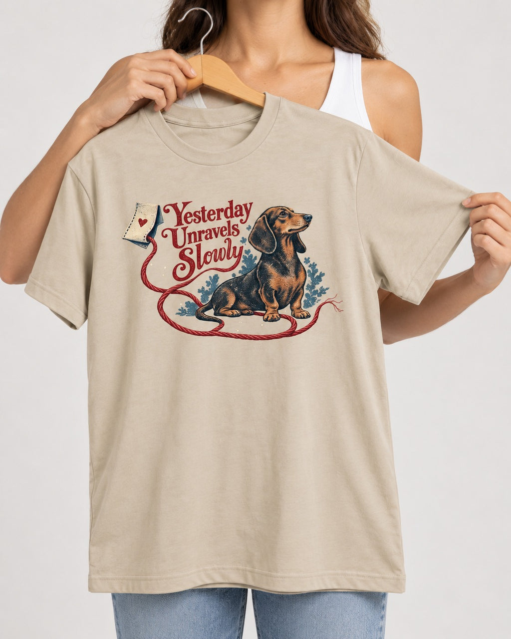 Yesterday Unravels Slowly with Dachshund T-Shirt in Sand, held up on a hanger