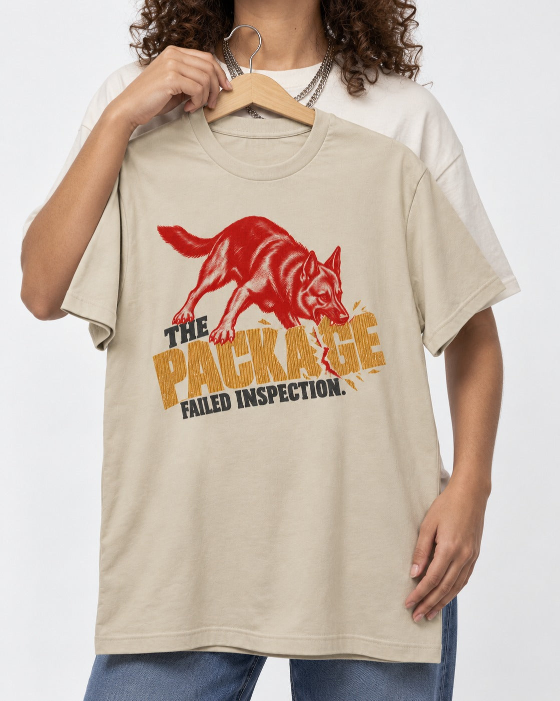 The Package Failed Inspection German Shepherd Dog T-Shirt in Sand, held up on a hanger