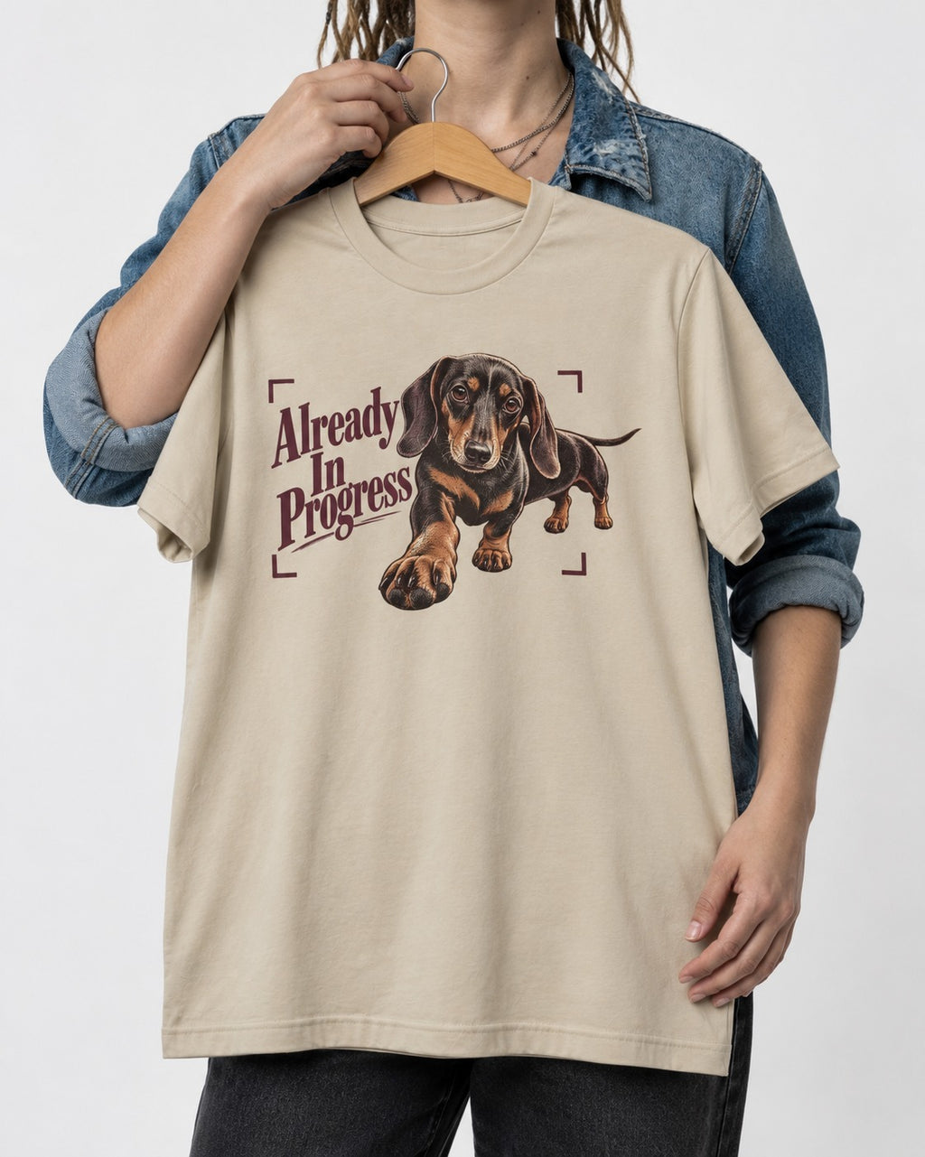 Dachshund Already in Progress T-Shirt in Sand, held up on a hanger