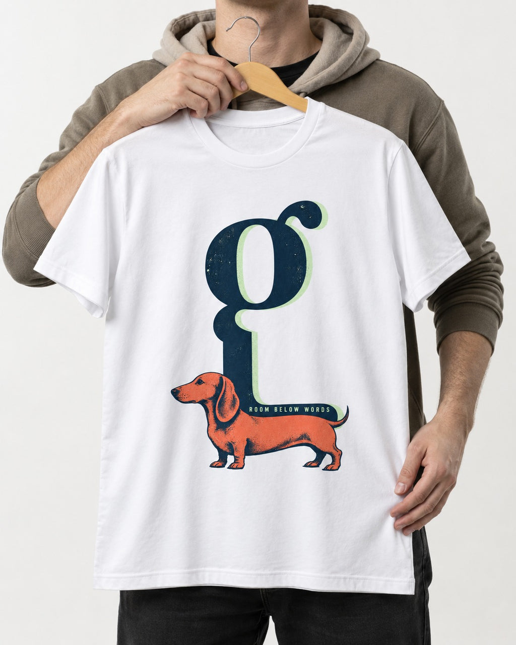 Dachshund Room Below Words Lowercase G Graphic T-Shirt in White, held up on a hanger