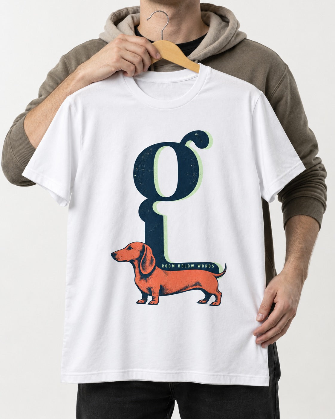 Dachshund Room Below Words Lowercase G Graphic T-Shirt in White, held up on a hanger
