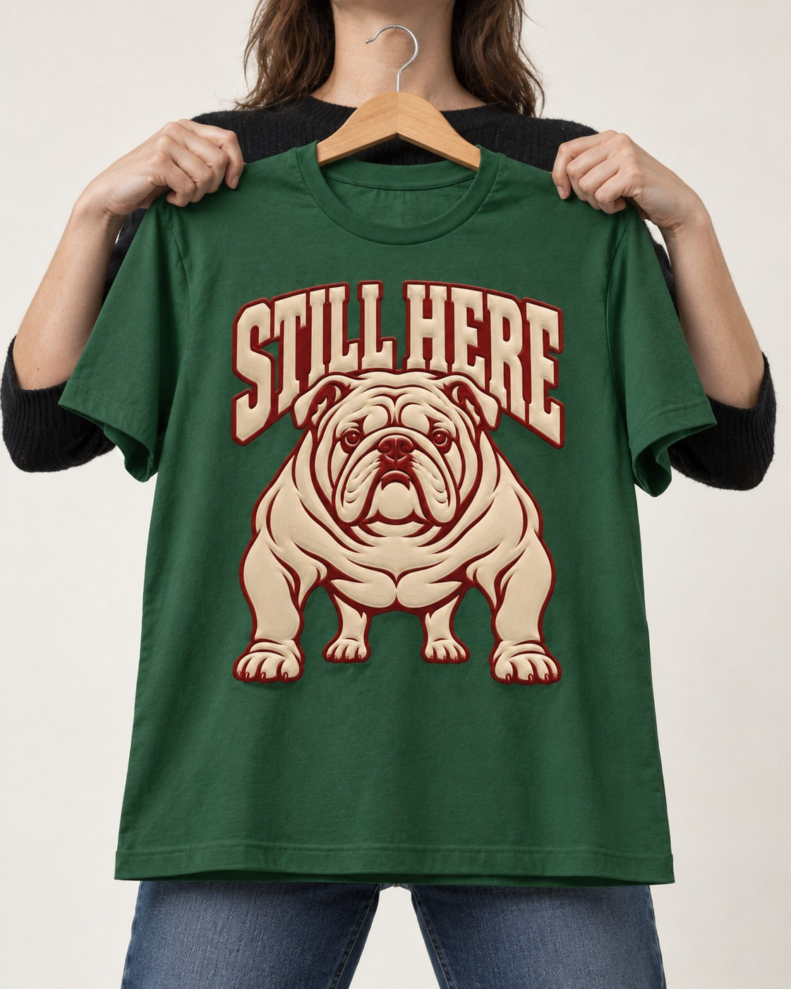 English Bulldog Still Here Collegiate Graphic T-Shirt in Forest Green, held up on a hanger