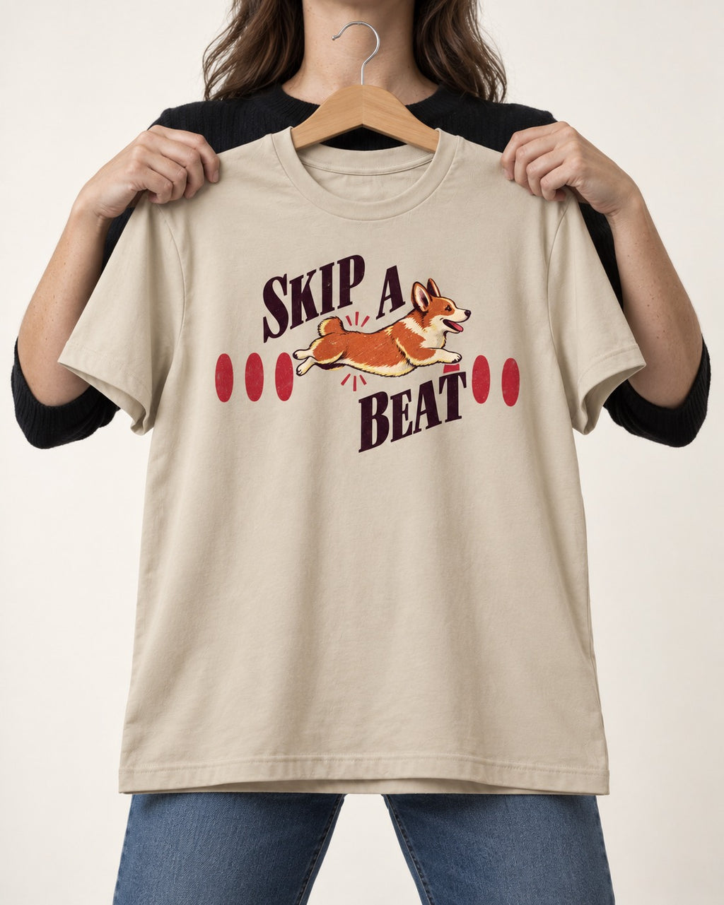 Skip a Beat Corgi T-Shirt in Sand, held up on a hanger