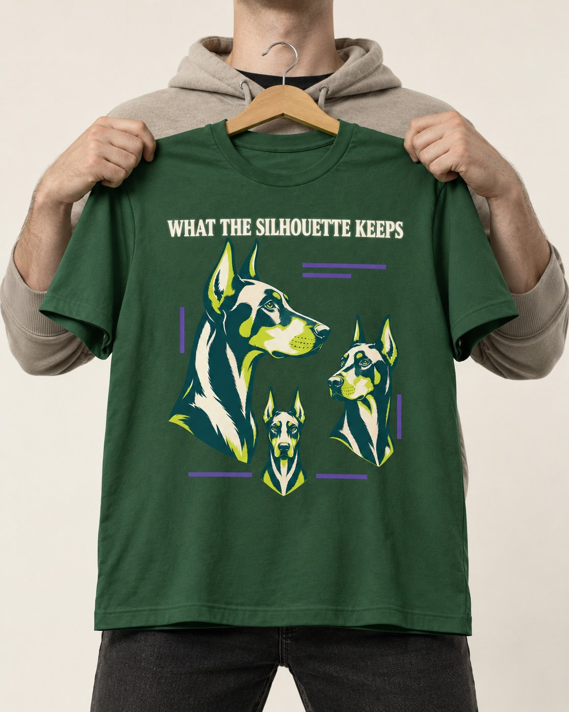 Doberman What the Silhouette Keeps Three Portrait Graphic T-Shirt in Forest Green, held up on a hanger