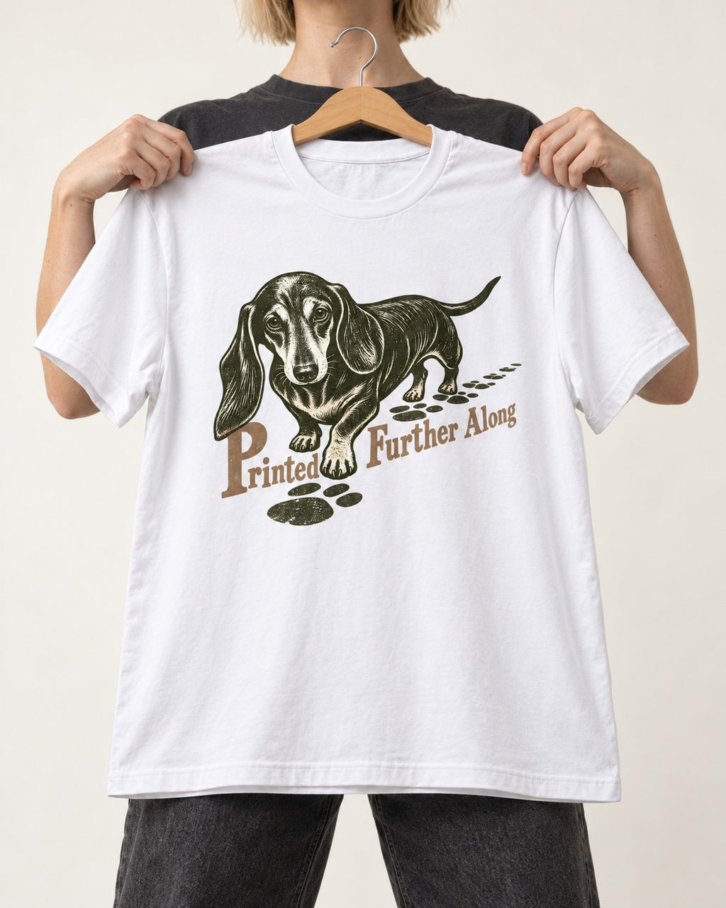 Dachshund Printed Further Along Footprint Graphic T-Shirt in White, held up on a hanger