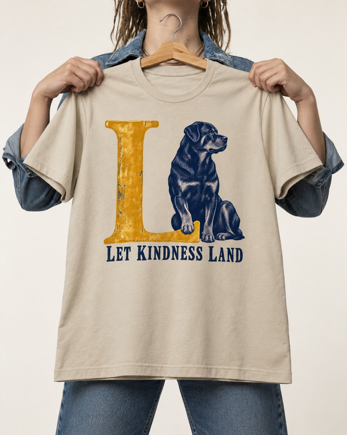 Let Kindness Lead Rottweiler T-Shirt in Sand, held up on a hanger
