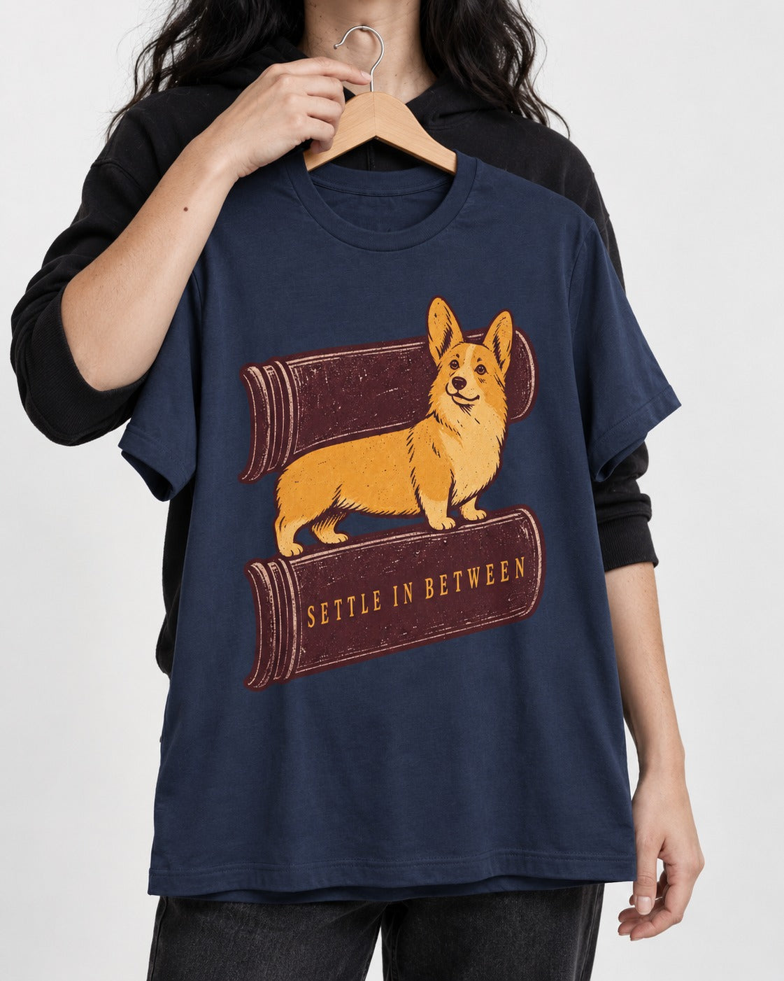Corgi Settle in Between T-Shirt in Navy, held up on a hanger
