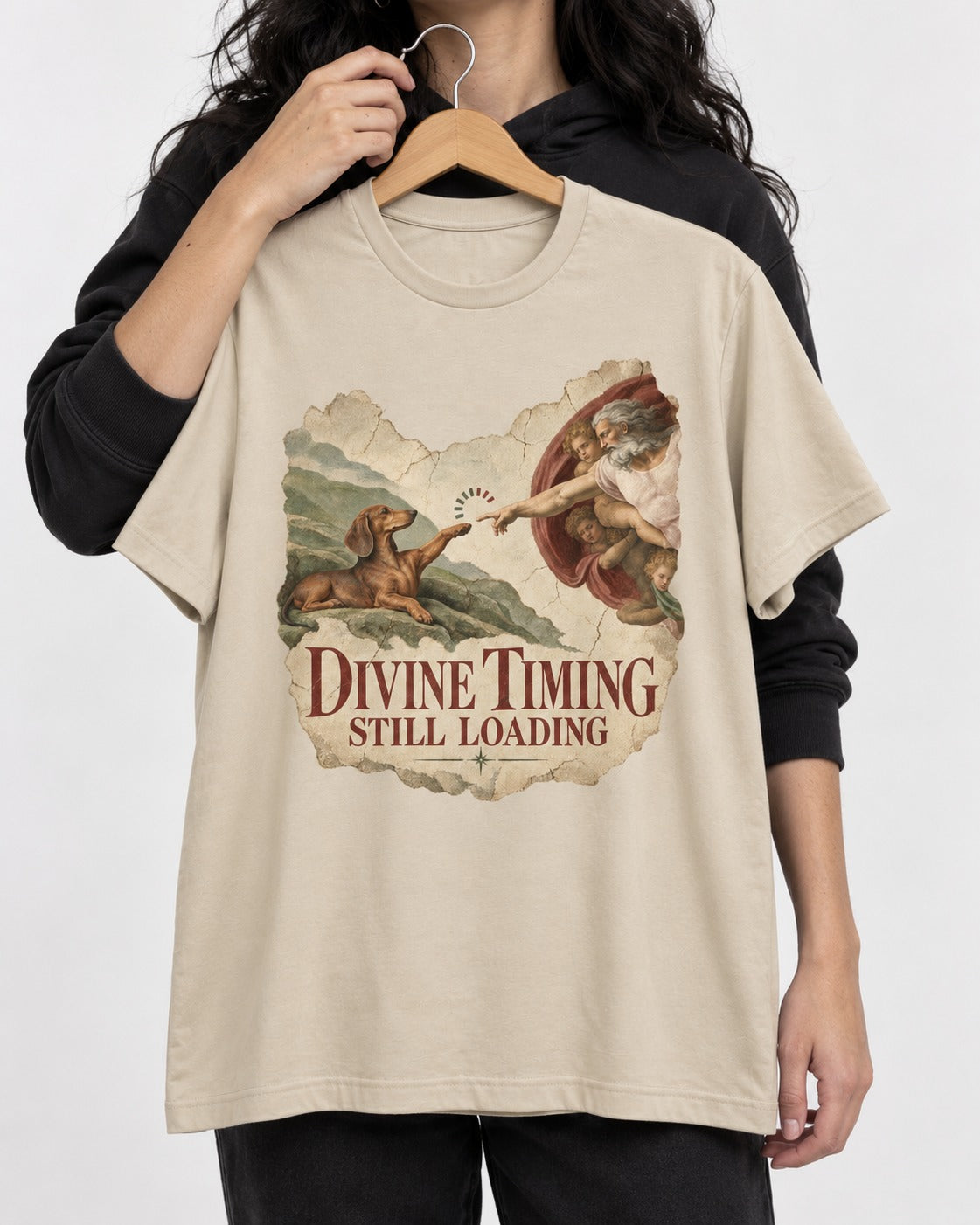 Dachshund's Divine Timing T-Shirt in Sand, held up on a hanger