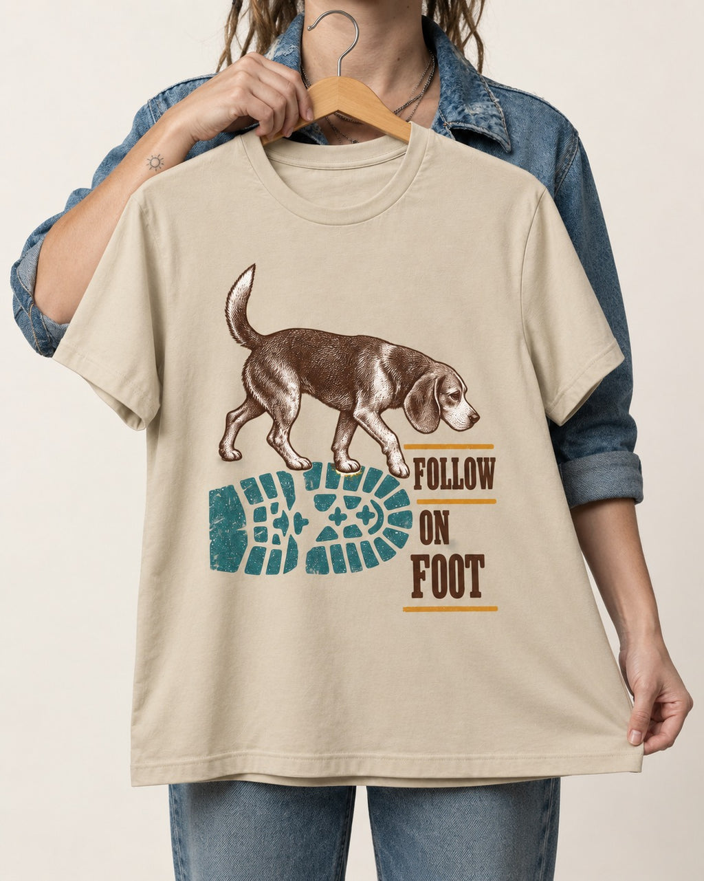 Follow the Beagle on Foot T-Shirt in Sand, held up on a hanger