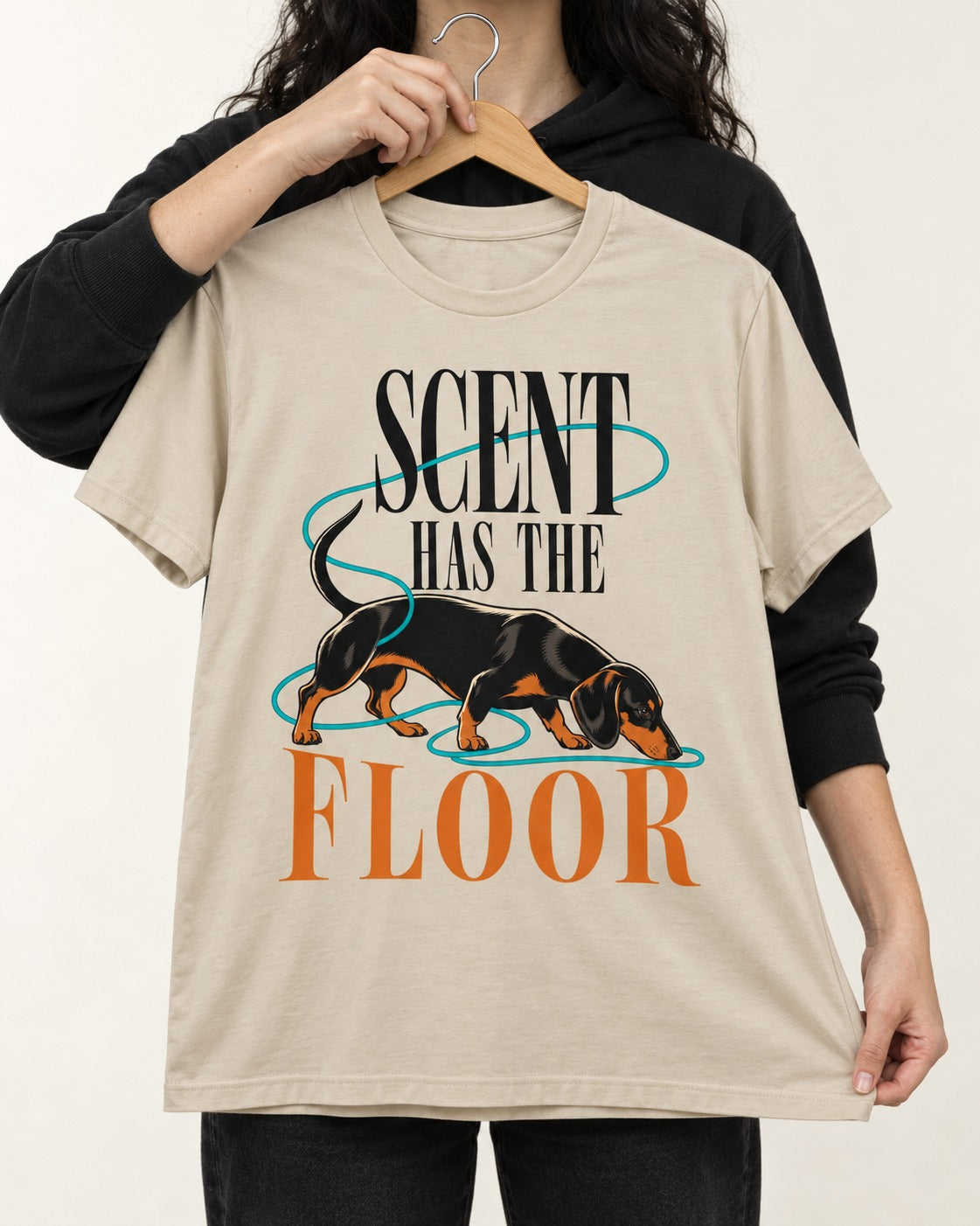 Dachshund Scent Has the Floor T-Shirt in Sand, held up on a hanger