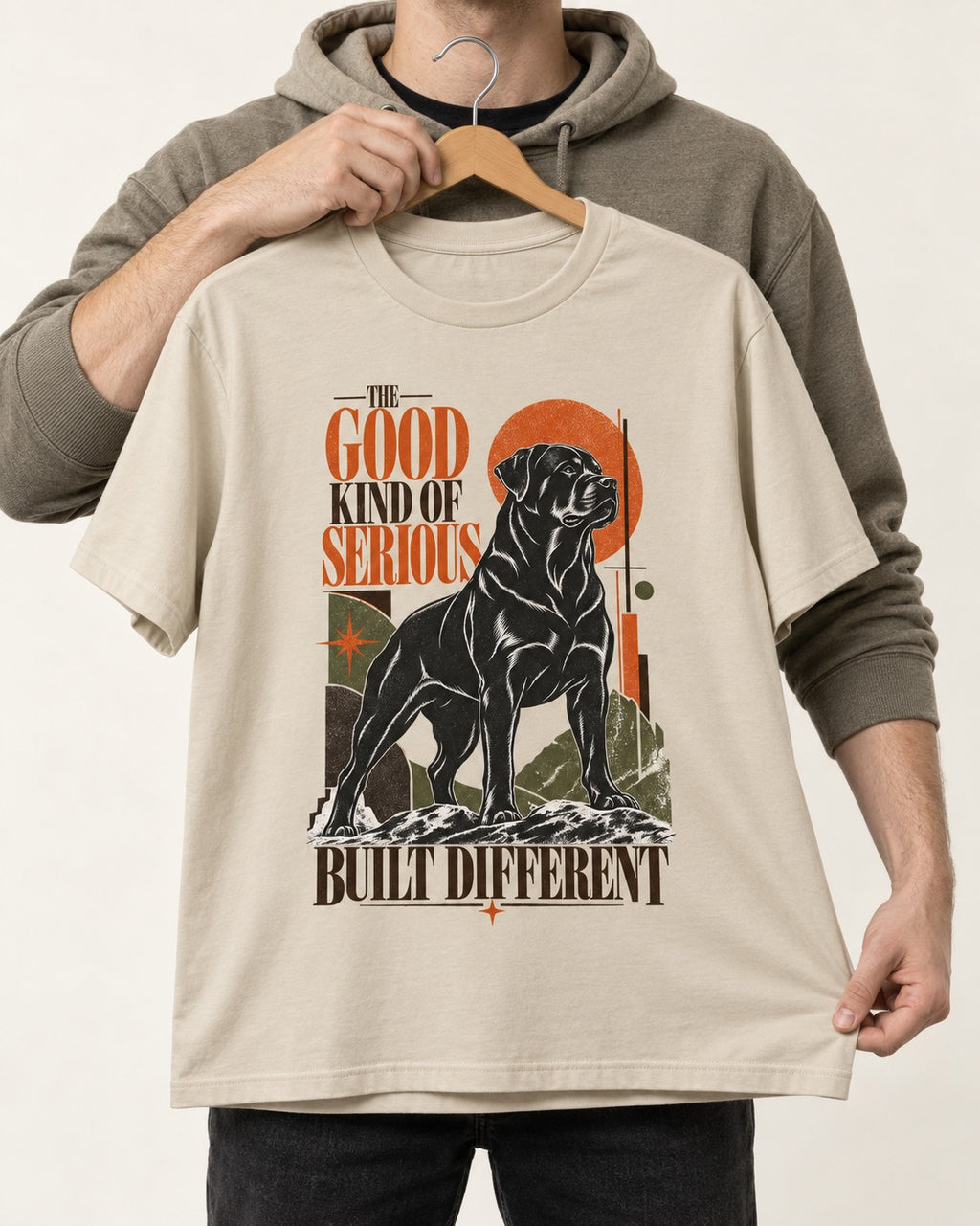 Rottweiler Built Different T-Shirt in Sand, held up on a hanger