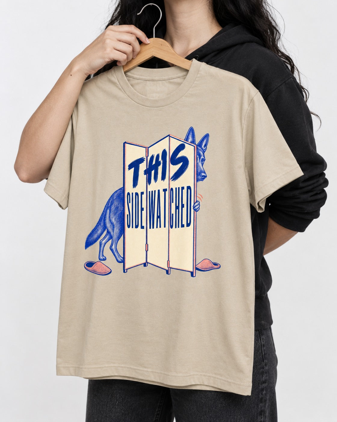 This Side Watched by German Shepherd Dog T-Shirt in Sand, held up on a hanger