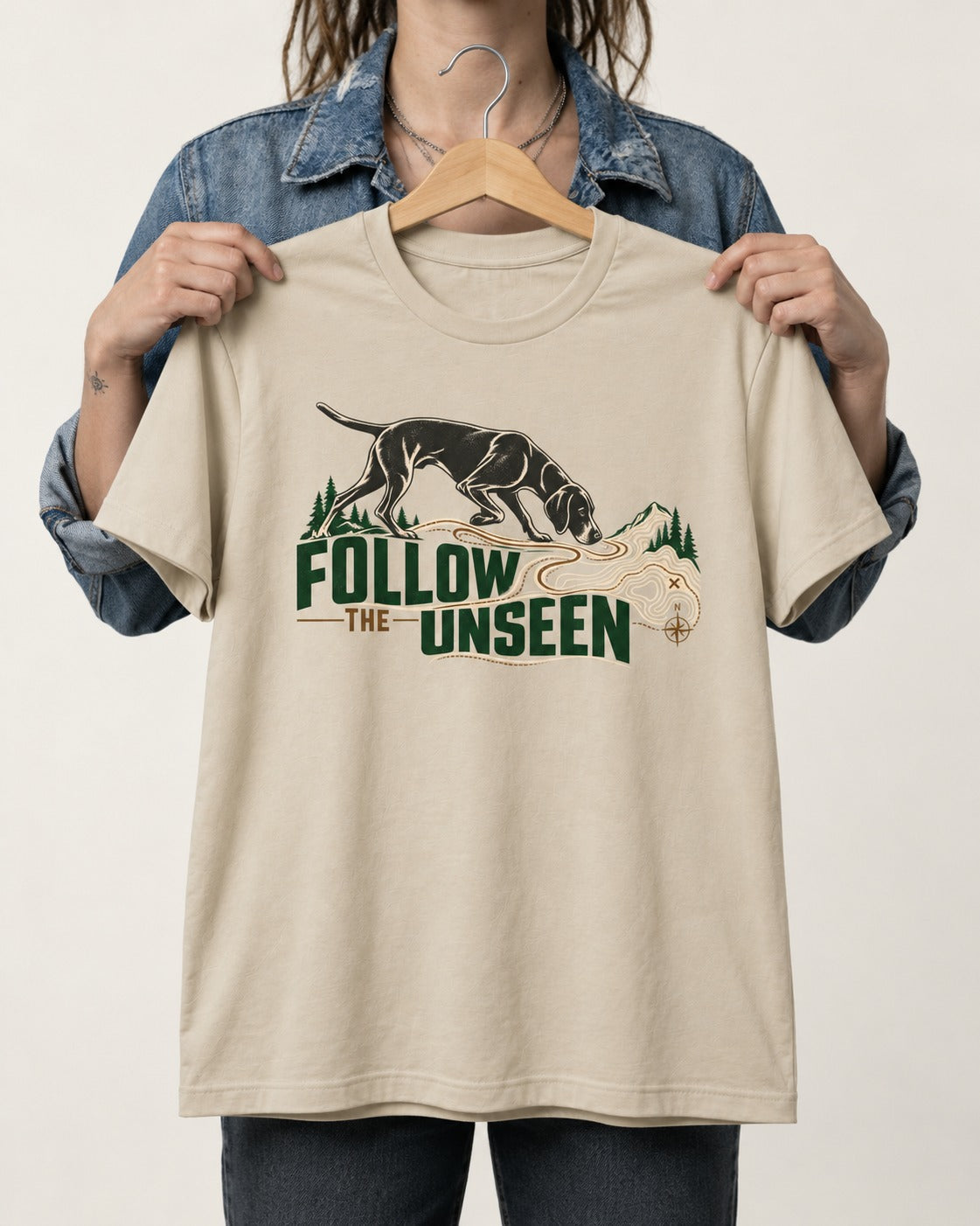 Follow the Unseen German Shorthaired Pointer T-Shirt in Sand, held up on a hanger