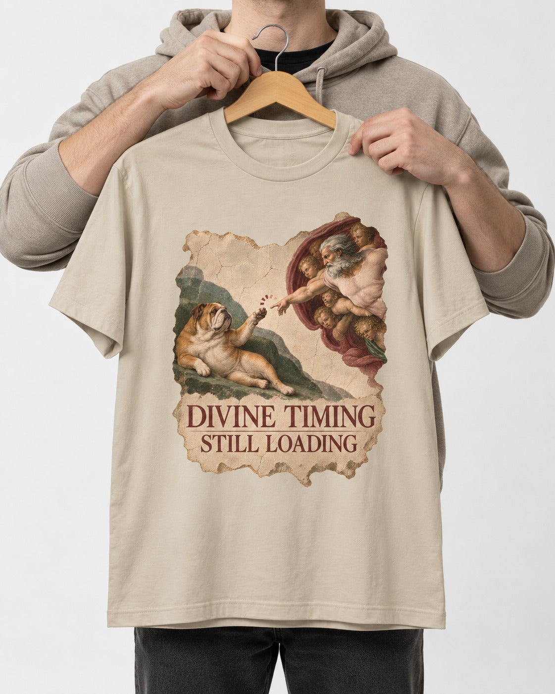 English Bulldog Divine Timing Still Loading T-Shirt in Sand, held up on a hanger