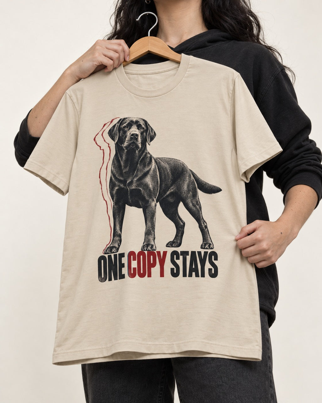 One Copy Stays Labrador Retriever T-Shirt in Sand, held up on a hanger