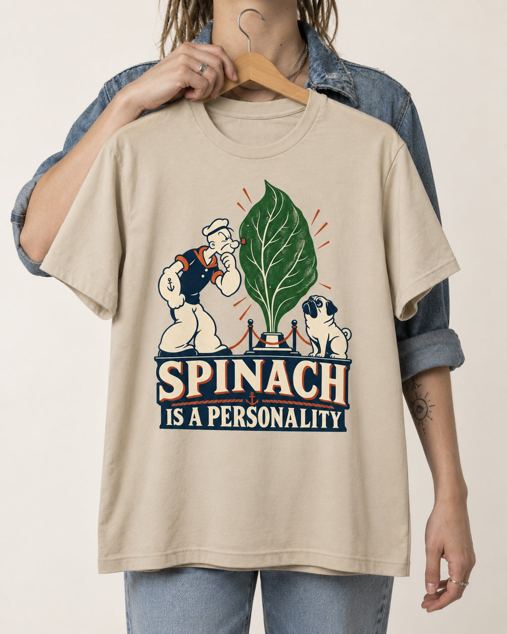 Pug Spinach Is a Personality T-Shirt in Sand, held up on a hanger