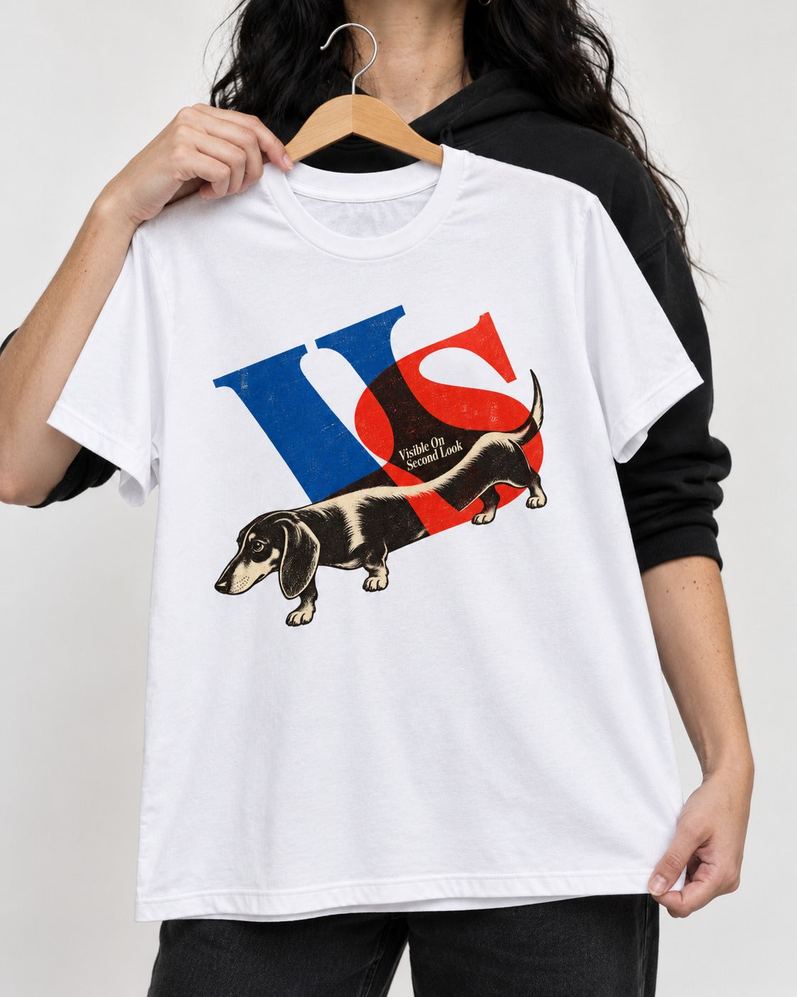 Dachshund VS Visible On Second Look Graphic T-Shirt in White, held up on a hanger