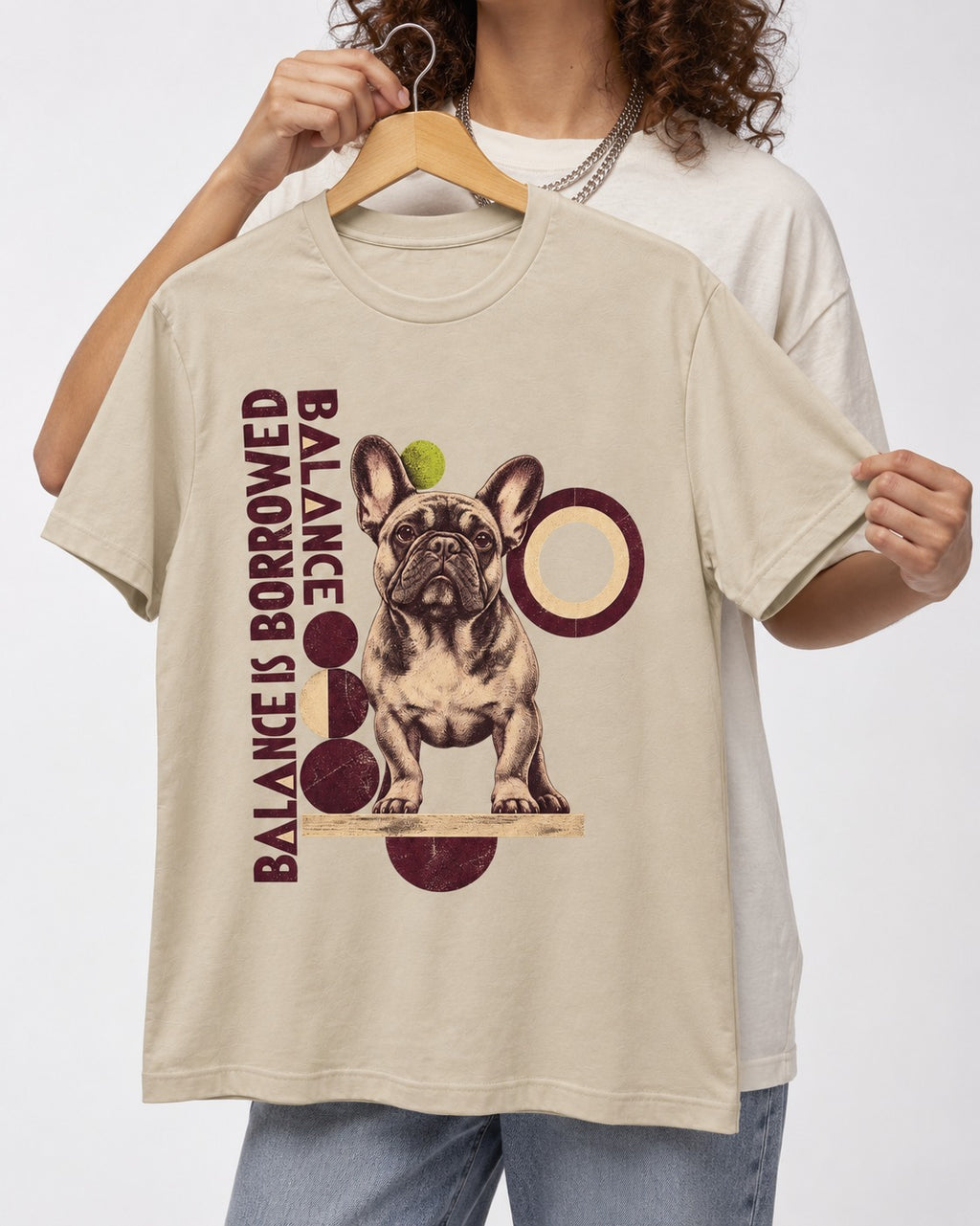Frenchie's Balance Is Borrowed T-Shirt in Sand, held up on a hanger