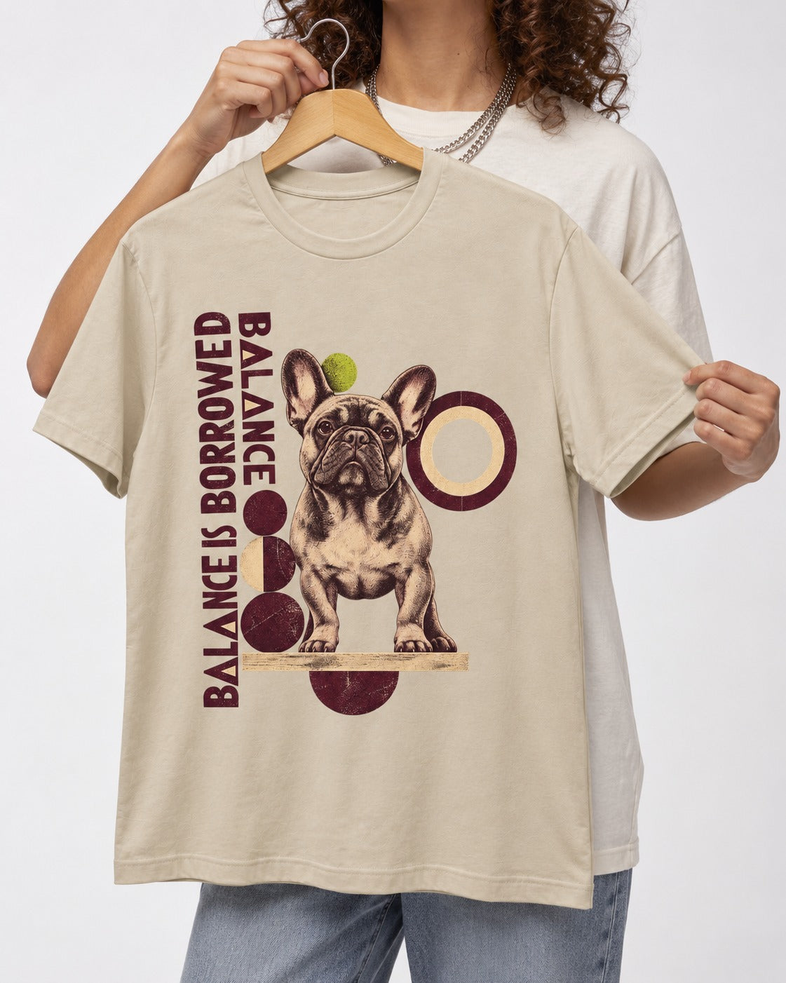 Frenchie's Balance Is Borrowed T-Shirt in Sand, held up on a hanger