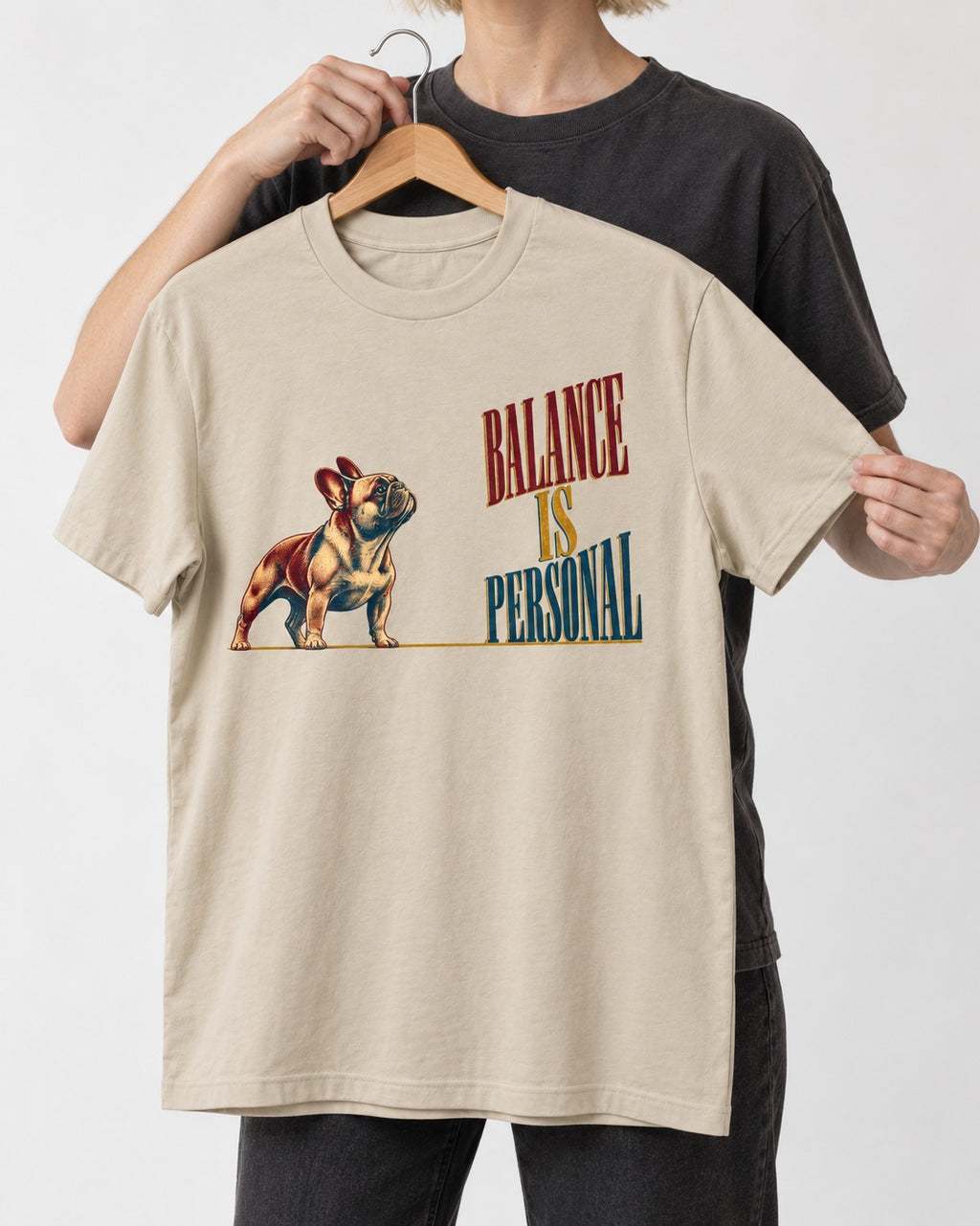 Frenchie Balance Is Personal T-Shirt in Sand, held up on a hanger