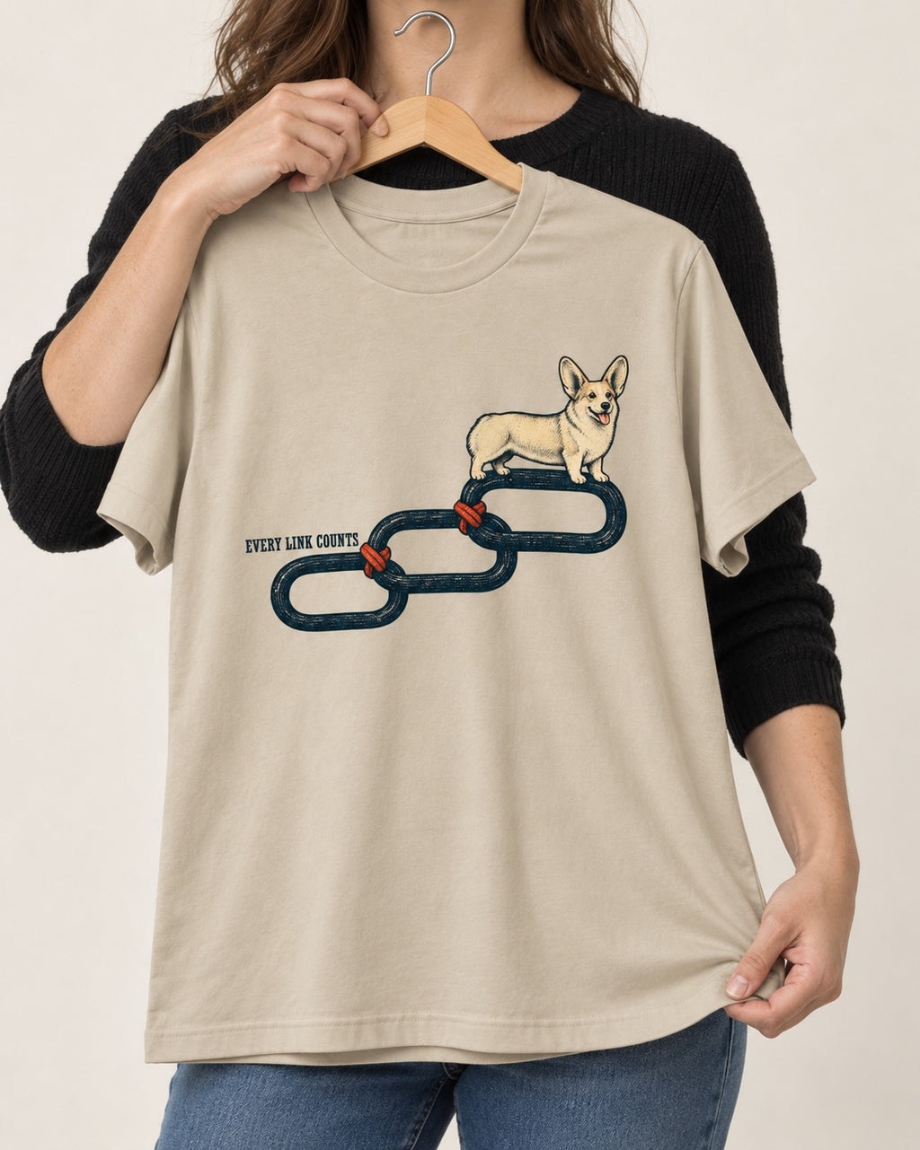 Every Corgi Link Counts T-Shirt in Sand, held up on a hanger