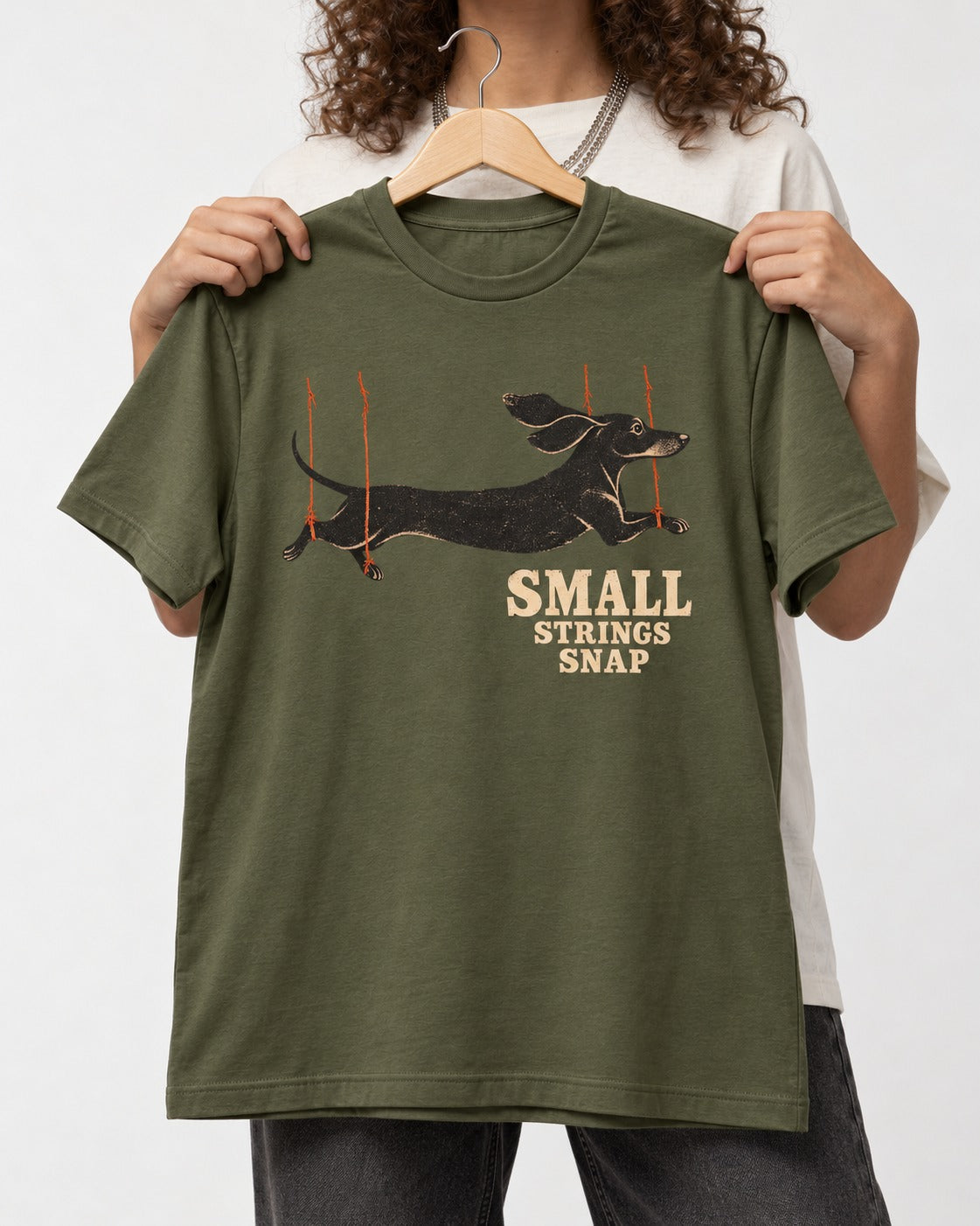Dachshund Small Strings Snap Marionette Graphic T-Shirt in Heather Military Green, held up on a hanger