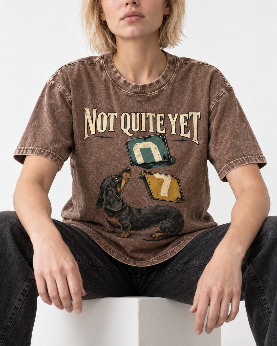 Not Quite Yet Dachshund Washed Tee in Coffee, worn by a seated model