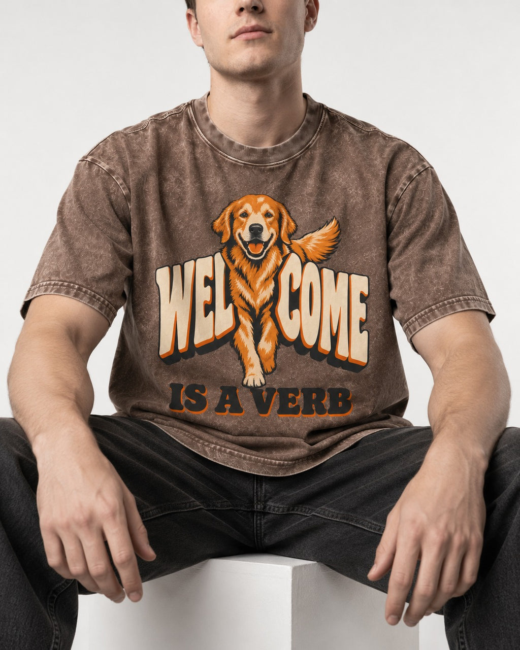 Golden Retriever Welcome Is a Verb Washed Tee in Coffee, worn by a seated model