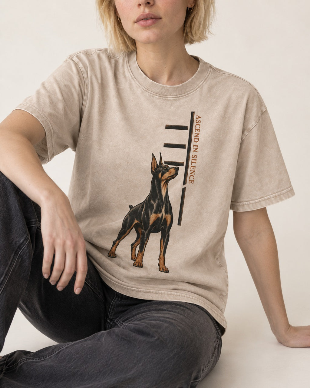 Doberman Ascend in Silence Washed Tee in Apricot, worn by a seated model