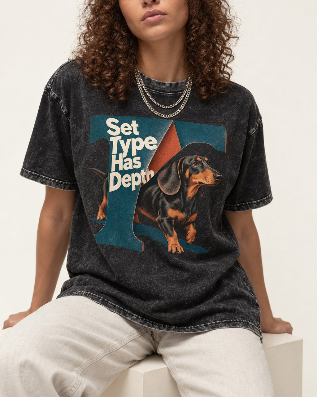 Dachshund Set Type Has Depth Folded Letter Graphic Washed Tee in Black, worn by a seated model