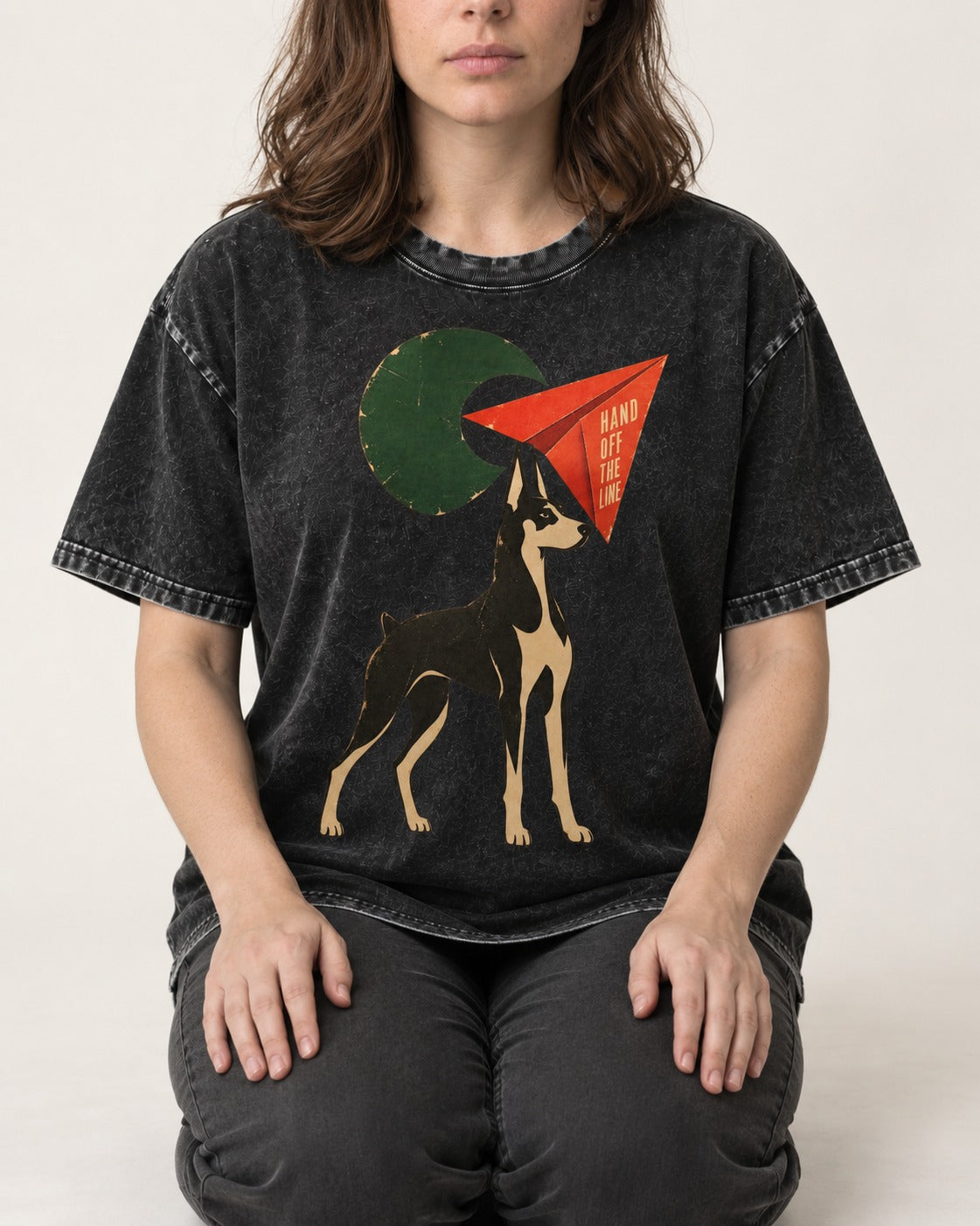 Doberman Hand Off the Line Paper Plane Graphic Washed Tee in Black, worn by a seated model
