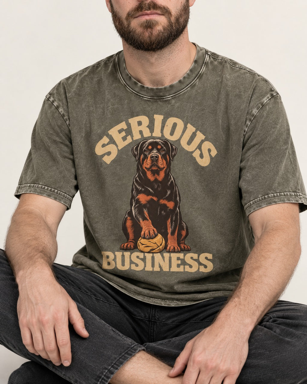 Rottweiler Serious Business Ball Under Paw Graphic Washed Tee in Army Green, worn by a seated model