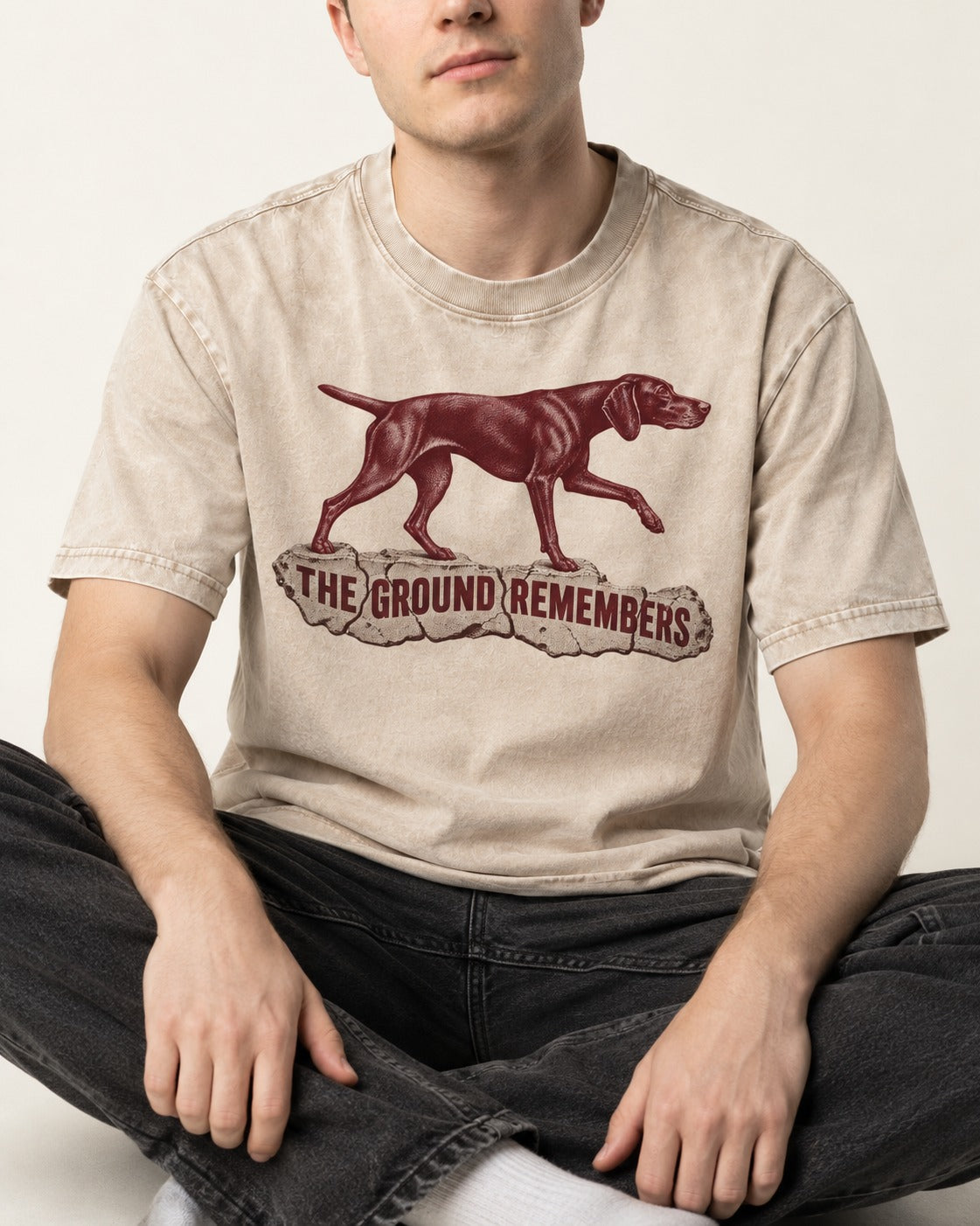 The Ground Remembers German Shorthaired Pointer Washed Tee in Apricot, worn by a seated model