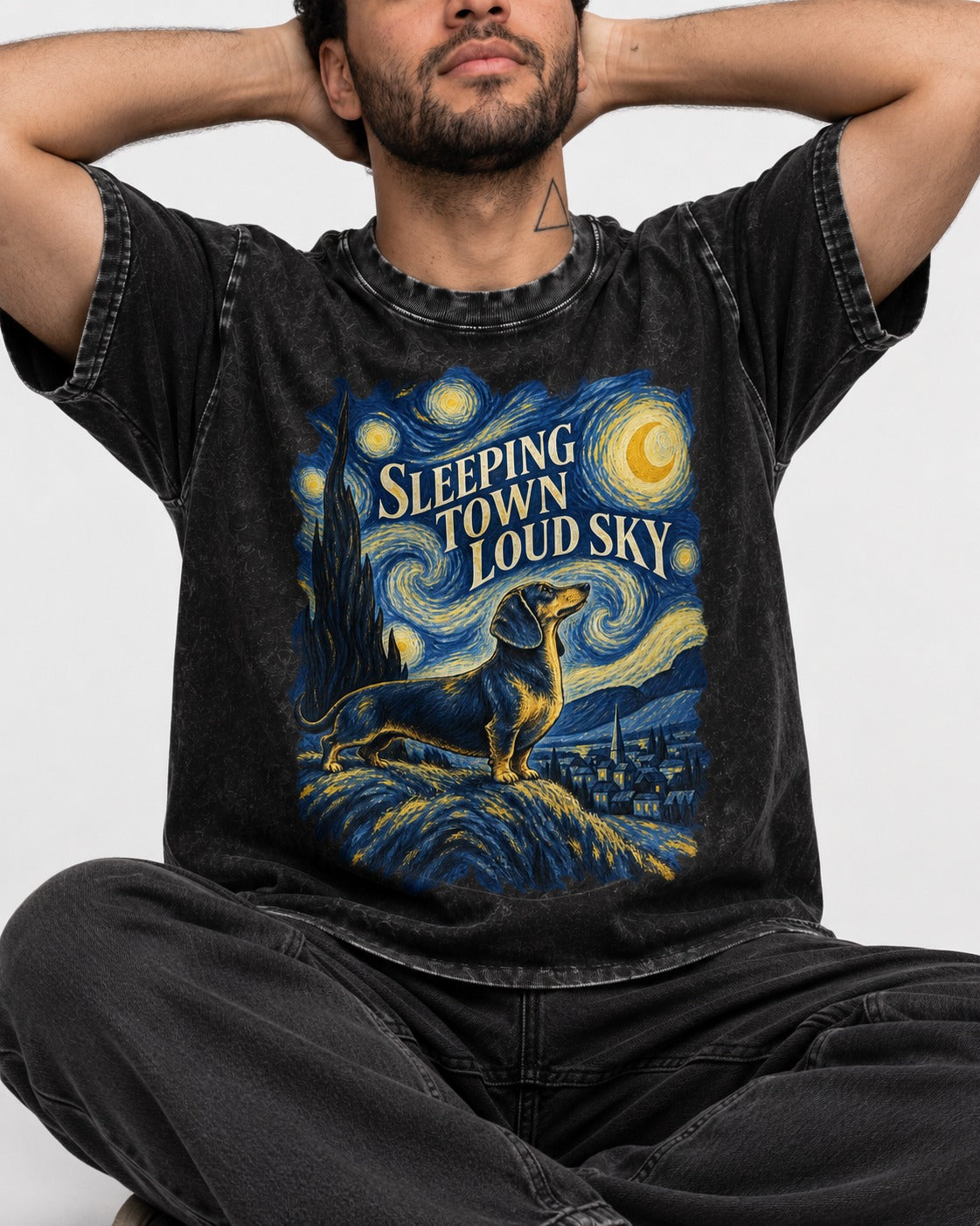 Dachshund Sleeping Town Loud Sky Starry Night Graphic Washed Tee in Black, worn by a seated model