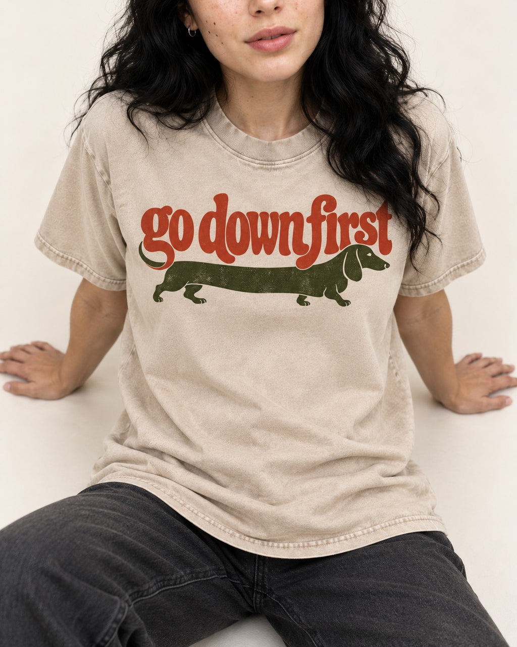 Dachshund Goes Down First Washed Tee in Apricot, worn by a seated model