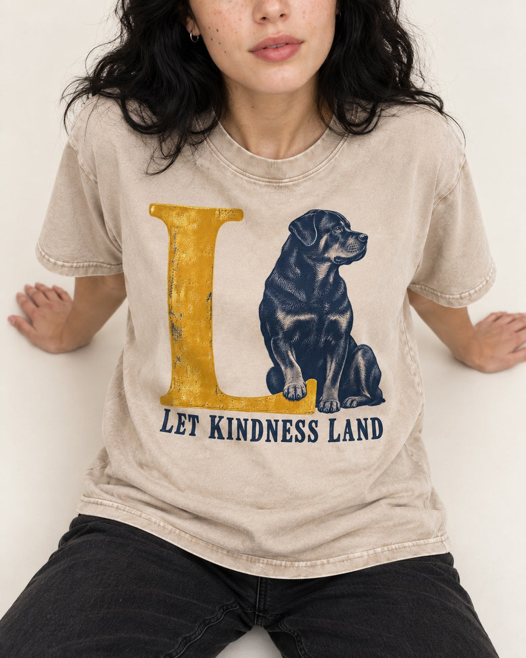 Let Kindness Lead Rottweiler Washed Tee in Apricot, worn by a seated model