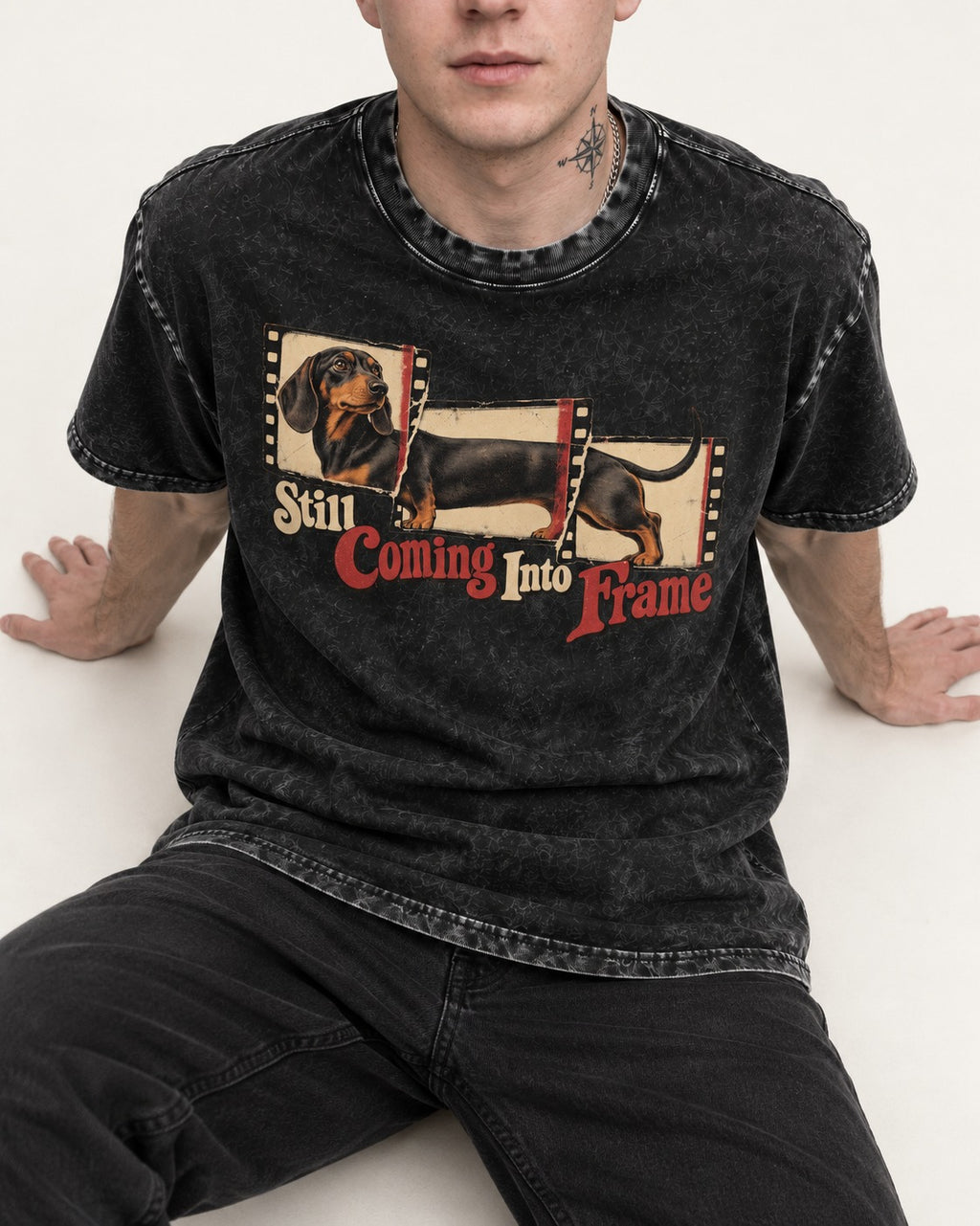 Dachshund Still Coming Into Frame Vintage Filmstrip Graphic Washed Tee in Black, worn by a seated model