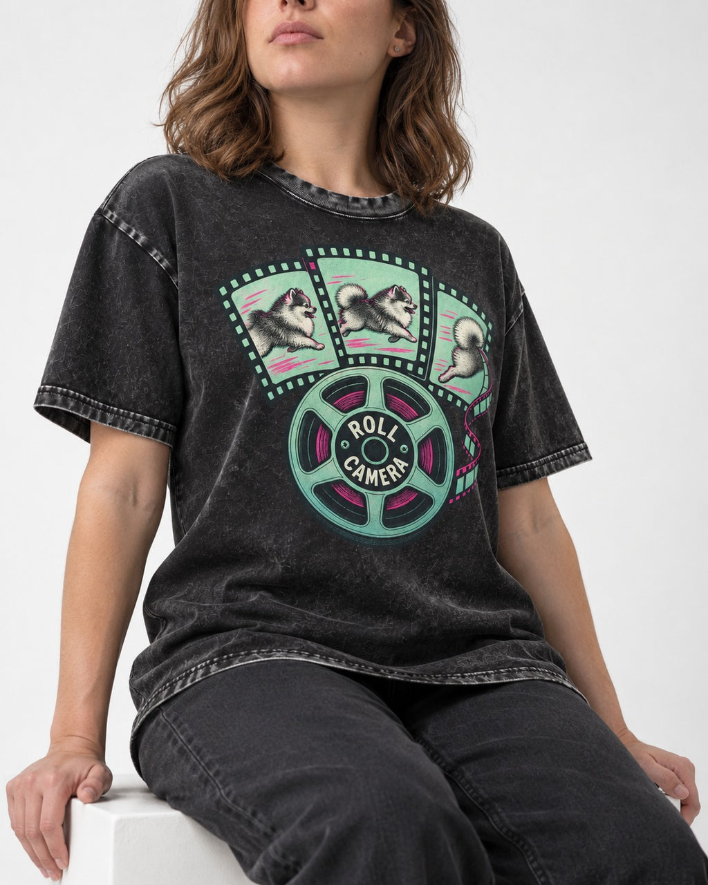 Pomeranian Roll Camera Film Reel Graphic Washed Tee in Black, worn by a seated model
