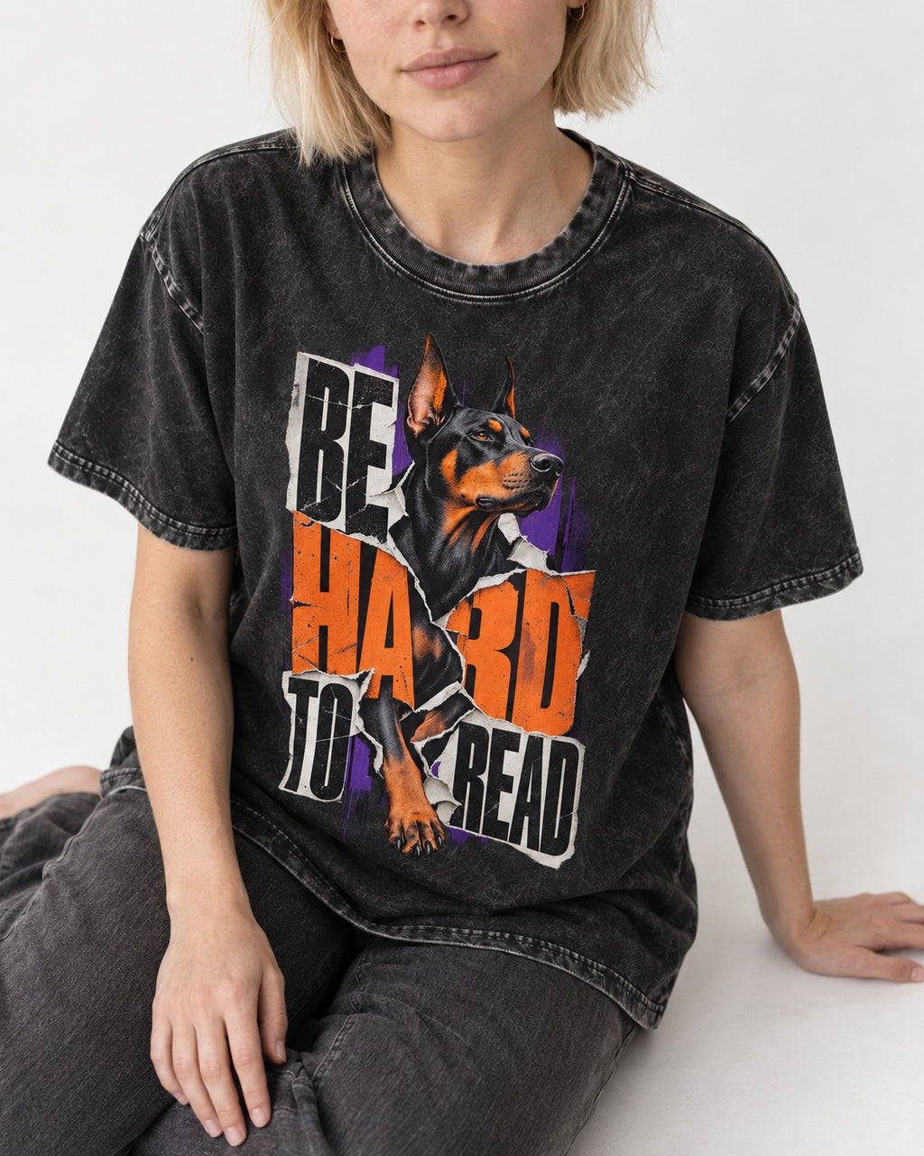 Doberman Be Hard to Read Torn Poster Graphic Washed Tee in Black, worn by a seated model