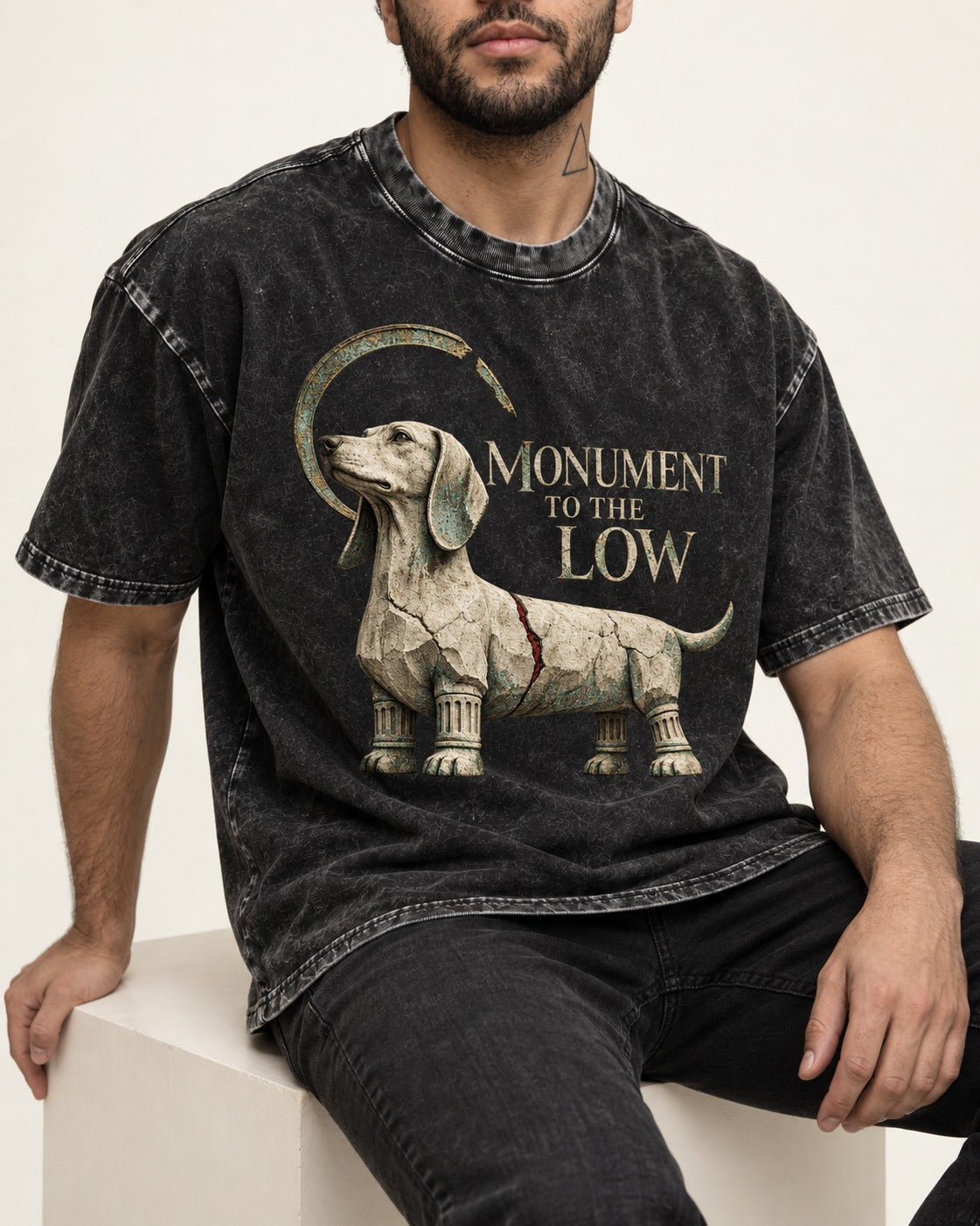 Dachshund Monument to the Low Stone Statue Graphic Washed Tee in Black, worn by a seated model