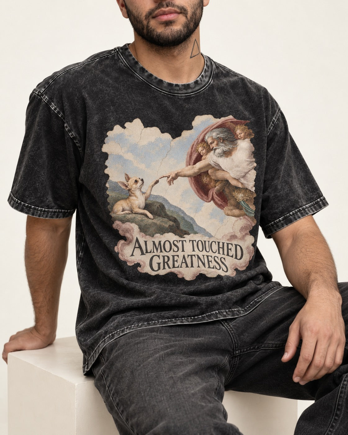 Chihuahua Almost Touched Greatness Renaissance Parody Washed Tee in Black, worn by a seated model