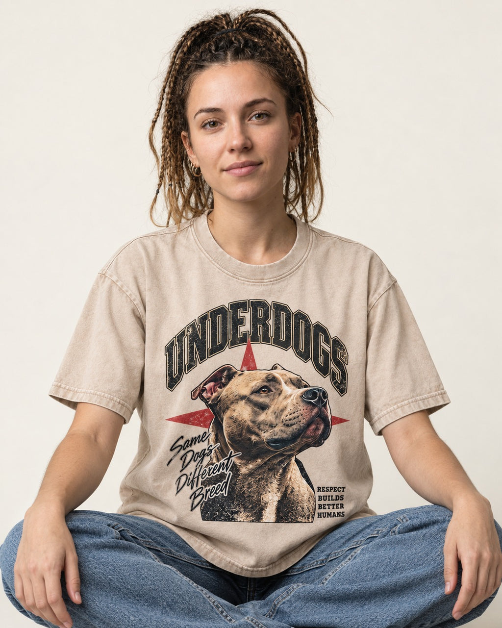Pitbull Underdogs Same Dogs Different Breed Portrait Graphic Washed Tee in Apricot, worn by a seated model
