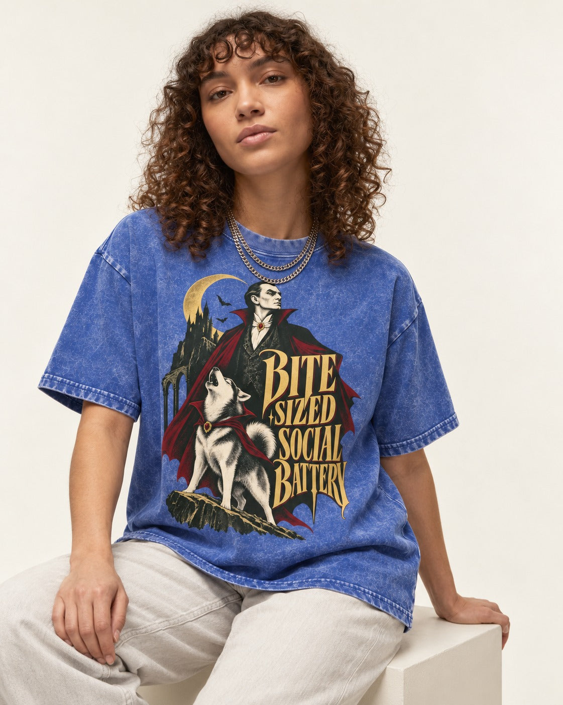 Husky Bite Sized Social Battery Vampire Graphic Washed Tee in Royal Blue, worn by a seated model